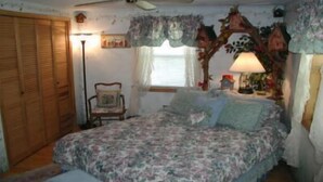 A bedroom with a floral bedspread, a wooden wardrobe, a chair, and a lamp.