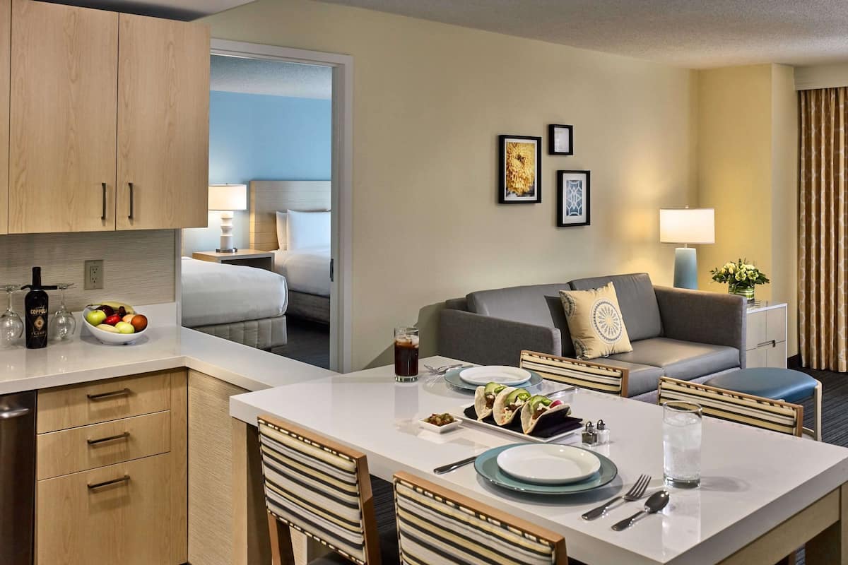 A hotel room with a kitchenette, a dining area, a sofa, and a bed.
