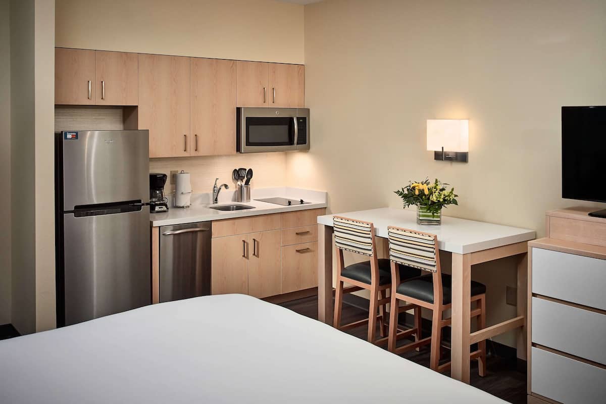 A compact hotel kitchen with a refrigerator, microwave, sink, and a small dining area with two chairs and a table.