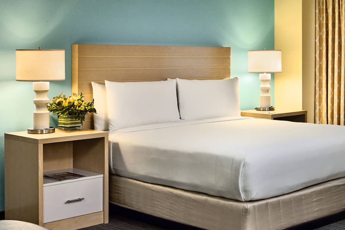 A hotel room with a large bed, two bedside tables, a nightstand, a drawer, and a small round table.