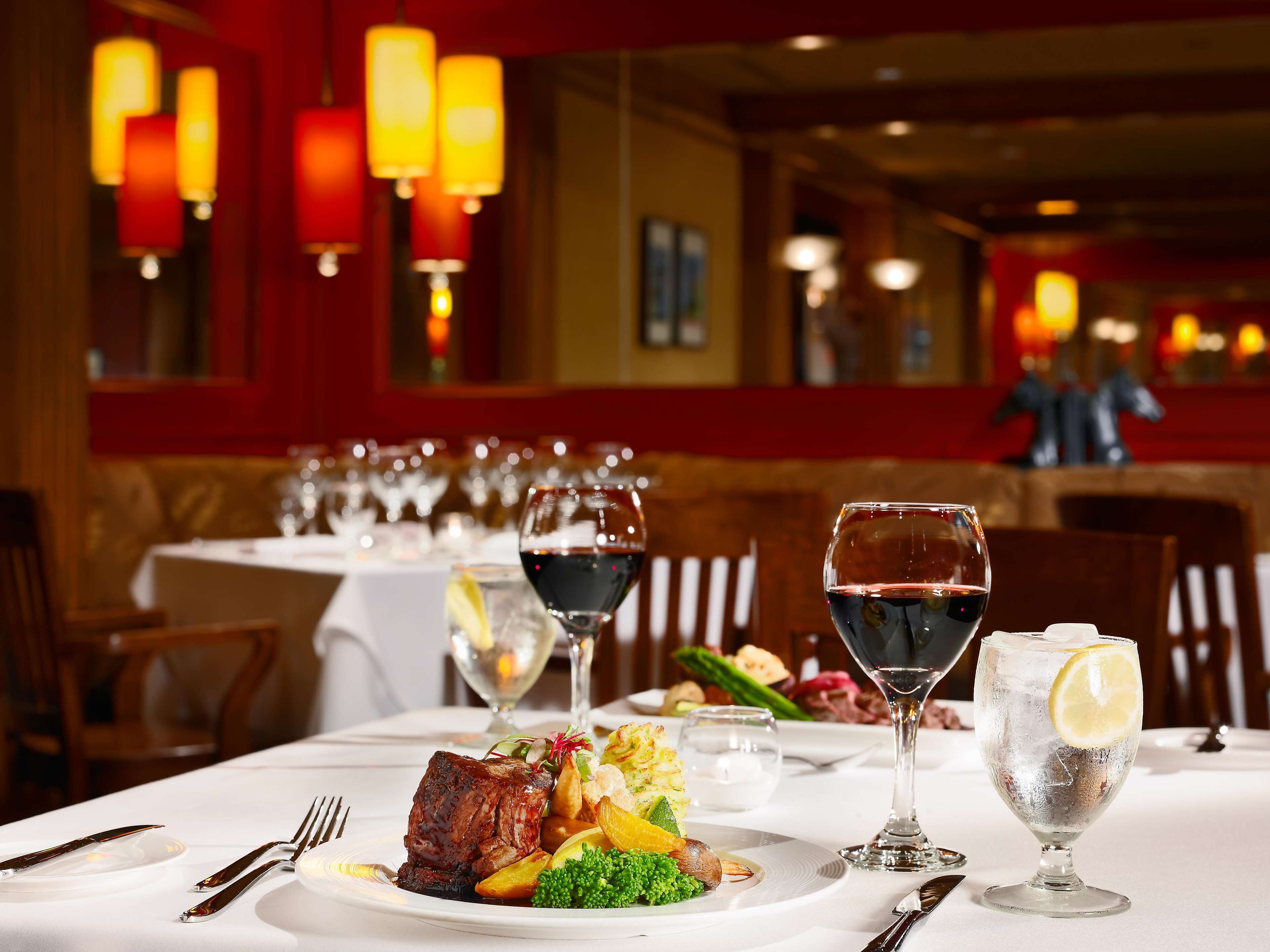 A restaurant table set with a steak, vegetables, and wine glasses.