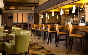 Un espace bar offrant différentes options de sièges, notamment des tabourets et des chaises de bar, un comptoir bien garni de bouteilles et de verres, et un éclairage suspendu.