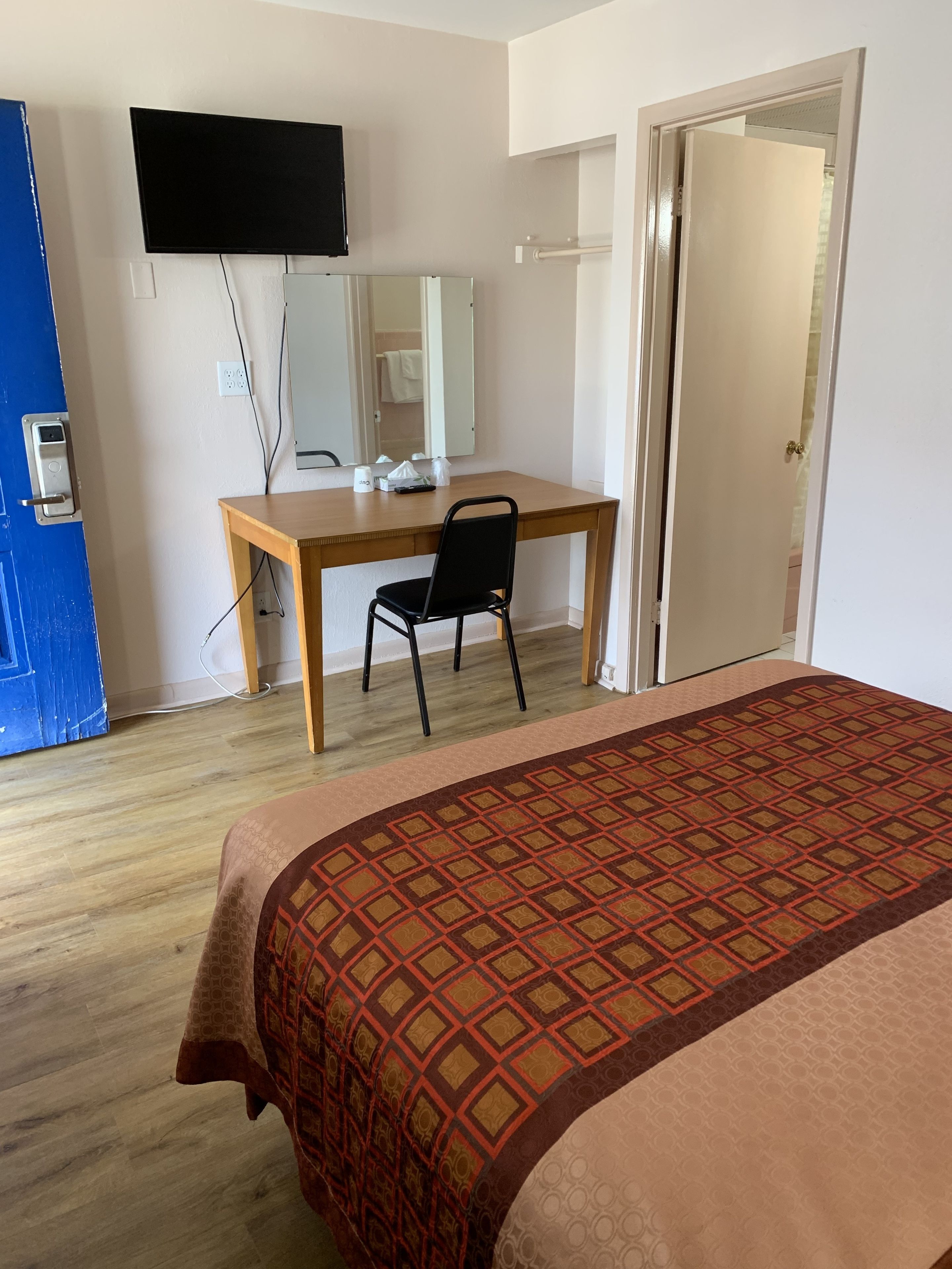 A hotel room with a bed, a desk, a chair, a television mounted on the wall, and a door leading to another room.