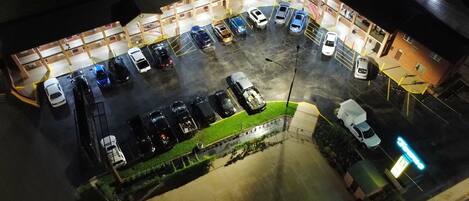 Vista aérea de un estacionamiento con varios autos y algunos camiones, rodeado de edificios con balcones.