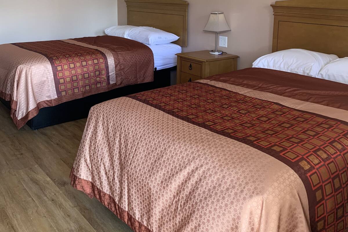 A hotel room with two beds, wooden headboards, a nightstand with a lamp, and a wooden floor.