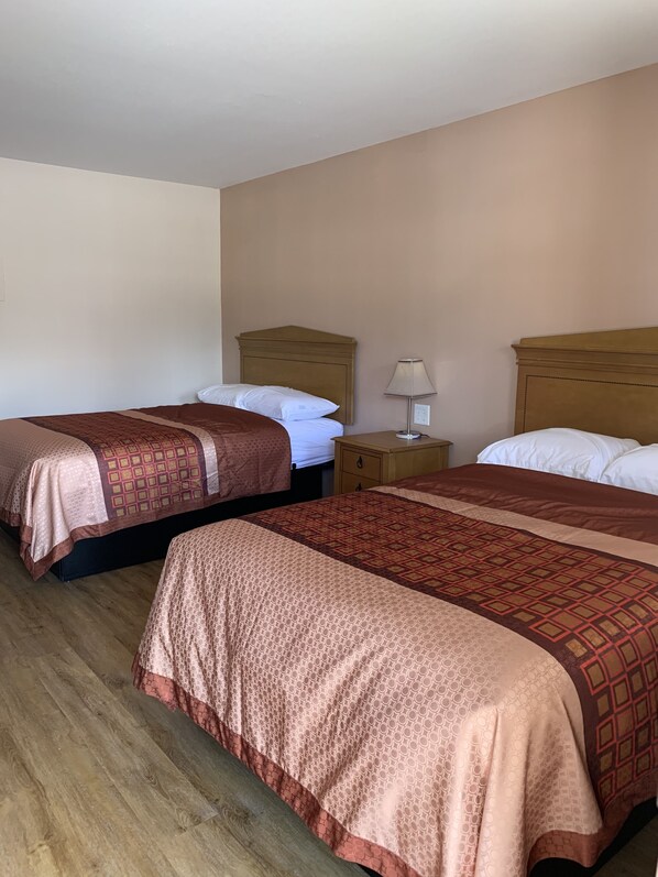 A hotel room with two beds, wooden headboards, a nightstand with a lamp, and a wooden floor.
