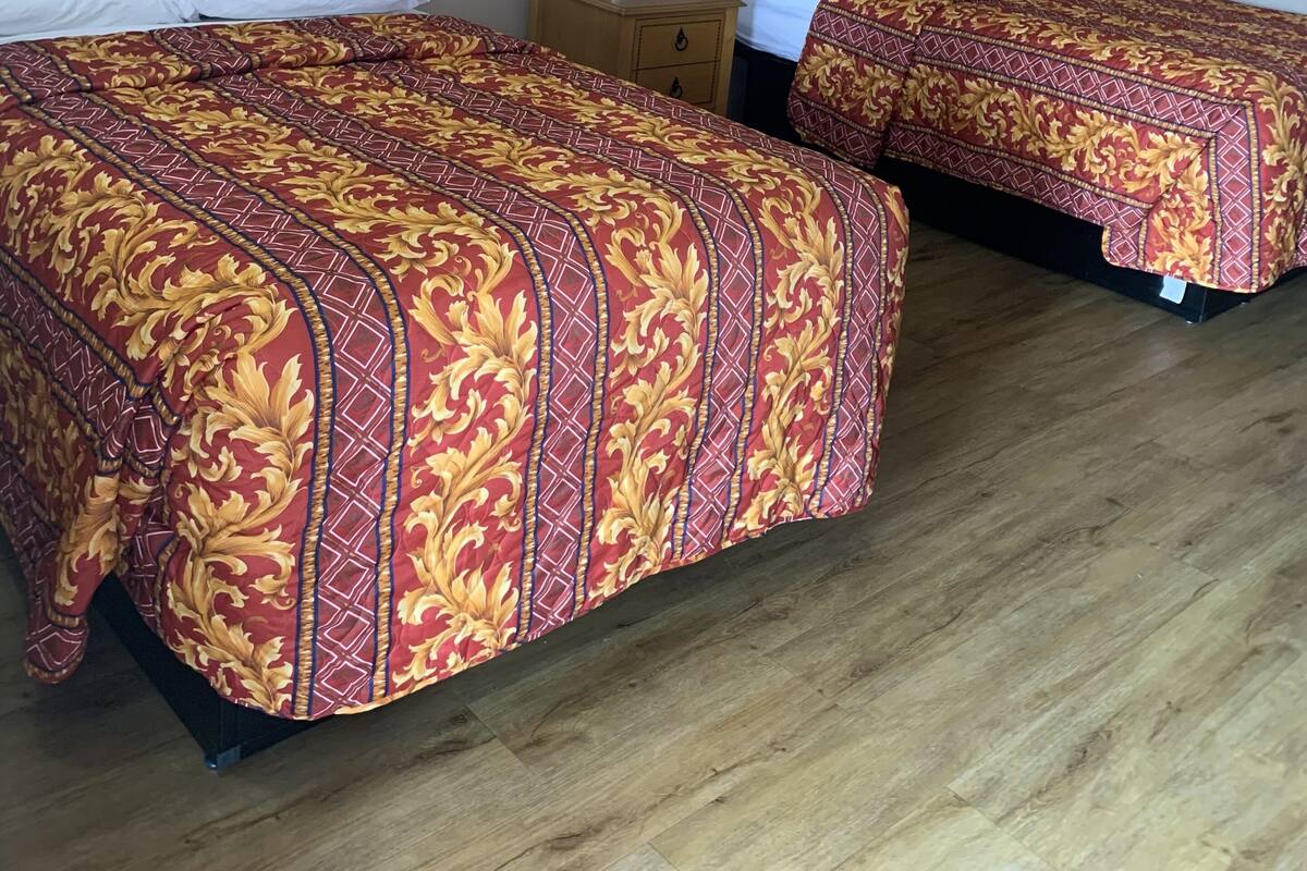 Two single beds with wooden headboards, a nightstand with a lamp, and a wooden floor.