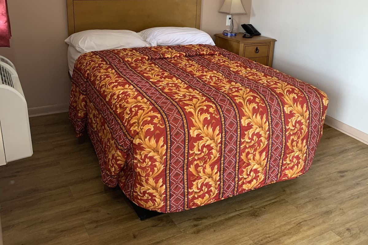 A bedroom with a wooden headboard, a patterned bedspread, a bedside table with a lamp, and a phone.
