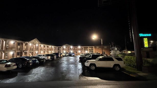 Fila de edificios de motel con varios espacios de estacionamiento y un letrero de neón.
