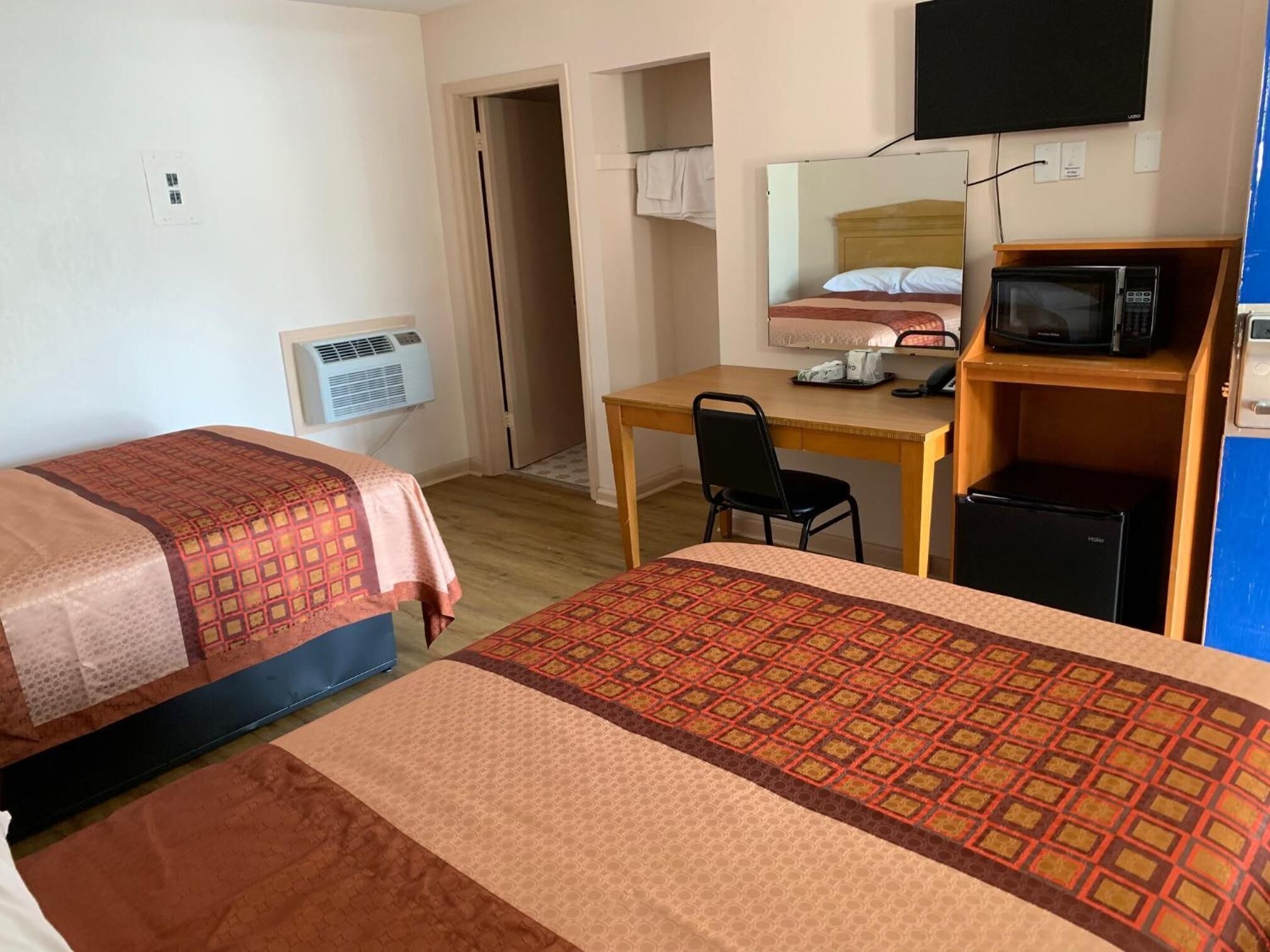 A hotel room with two beds, a desk, a chair, a television, and a small refrigerator.