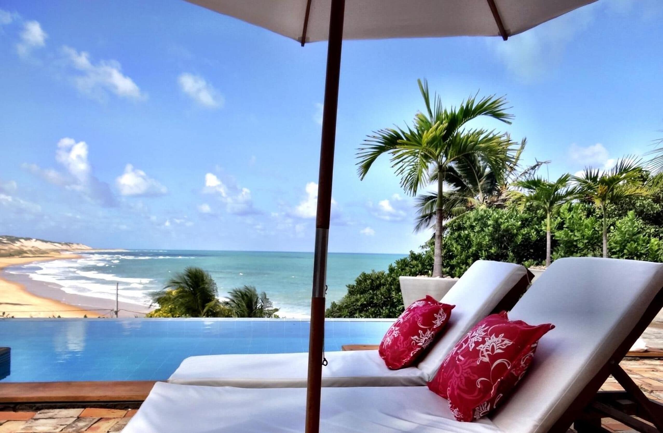 A poolside lounge with two sunbeds and a beach view.