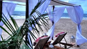 A beach setting with a canopy, two wooden lounge chairs with cushions, and a lantern. - Pousada Sagi Iti (Baia Formosa)