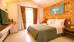 A bedroom with a bed, a television, a brick wall, and a door leading to a balcony. - Pousada Sagi Iti (Baia Formosa)