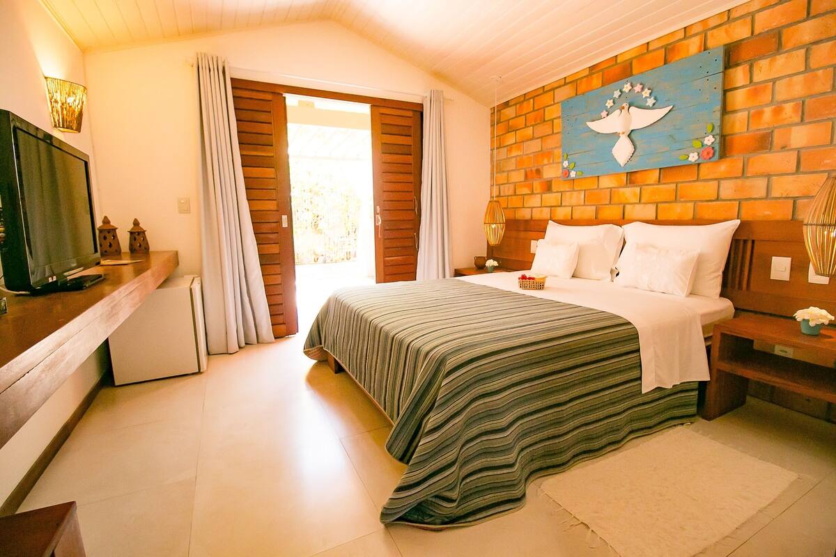 A bedroom with a bed, a television, a brick wall, and a door leading to a balcony.