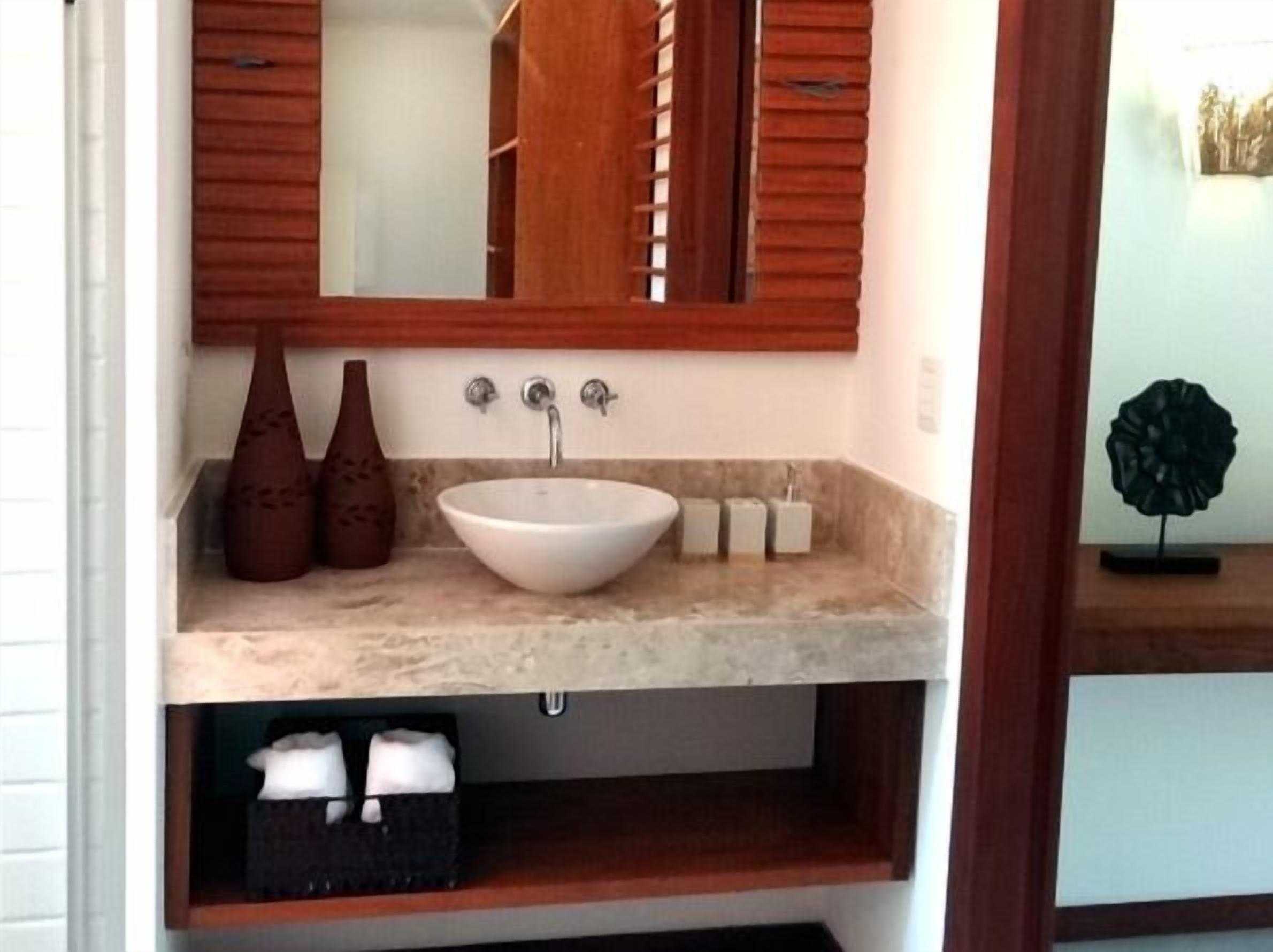 A bathroom with a white sink, two brown vases, a mirror, and a wooden cabinet.