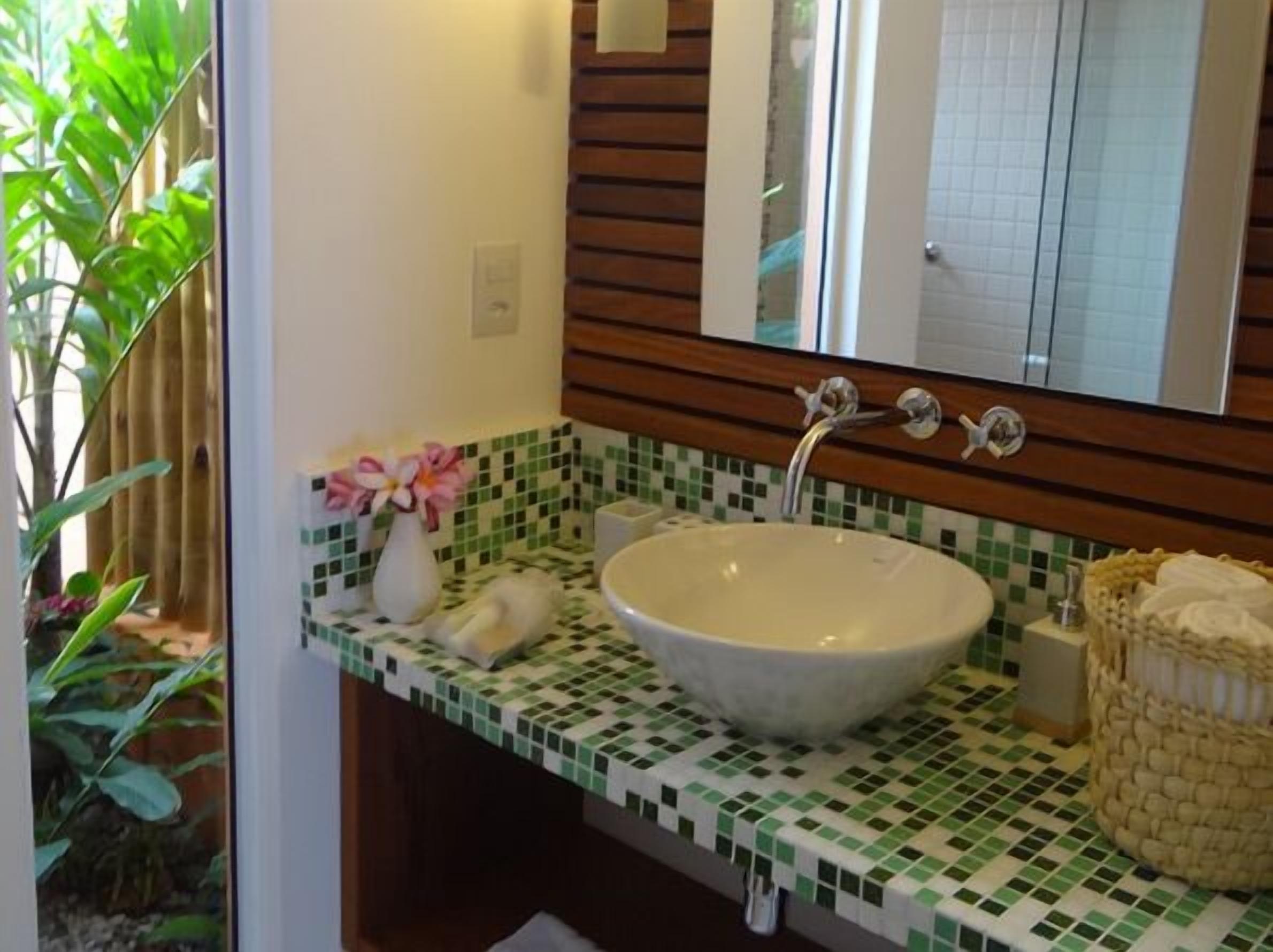 Een badkamer met een witte wastafel, groen-wit geruit tegels, een houten paneel boven de wastafel en een spiegel.