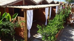 A row of wooden cabins with white curtains, surrounded by lush greenery and palm trees. - Pousada Sagi Iti (Baia Formosa)