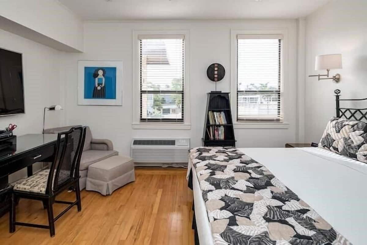 Ein Schlafzimmer mit Bett, Schreibtisch, Stuhl, Bücherregal und einem Fenster mit Jalousien.