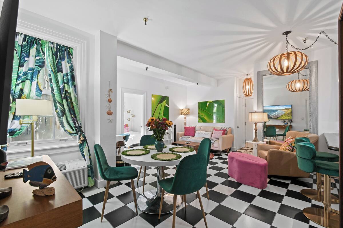 Ein modernes Wohnzimmer mit einem Schachbrettmuster-Boden, grünen und rosafarbenen Möbeln und einem Essbereich mit einem runden Tisch und Stühlen.
