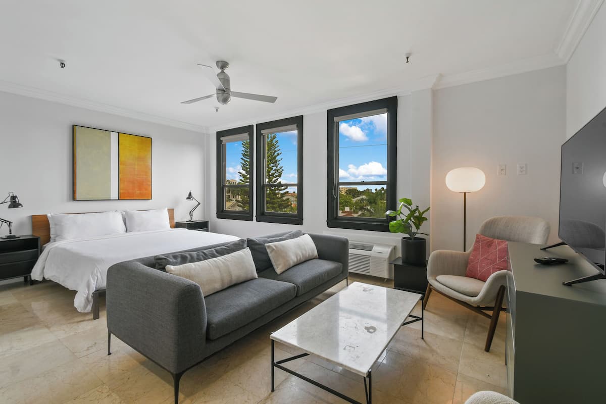 Ein modernes Hotelzimmer mit Bett, grauem Sofa, weißem Couchtisch und Fernseher.