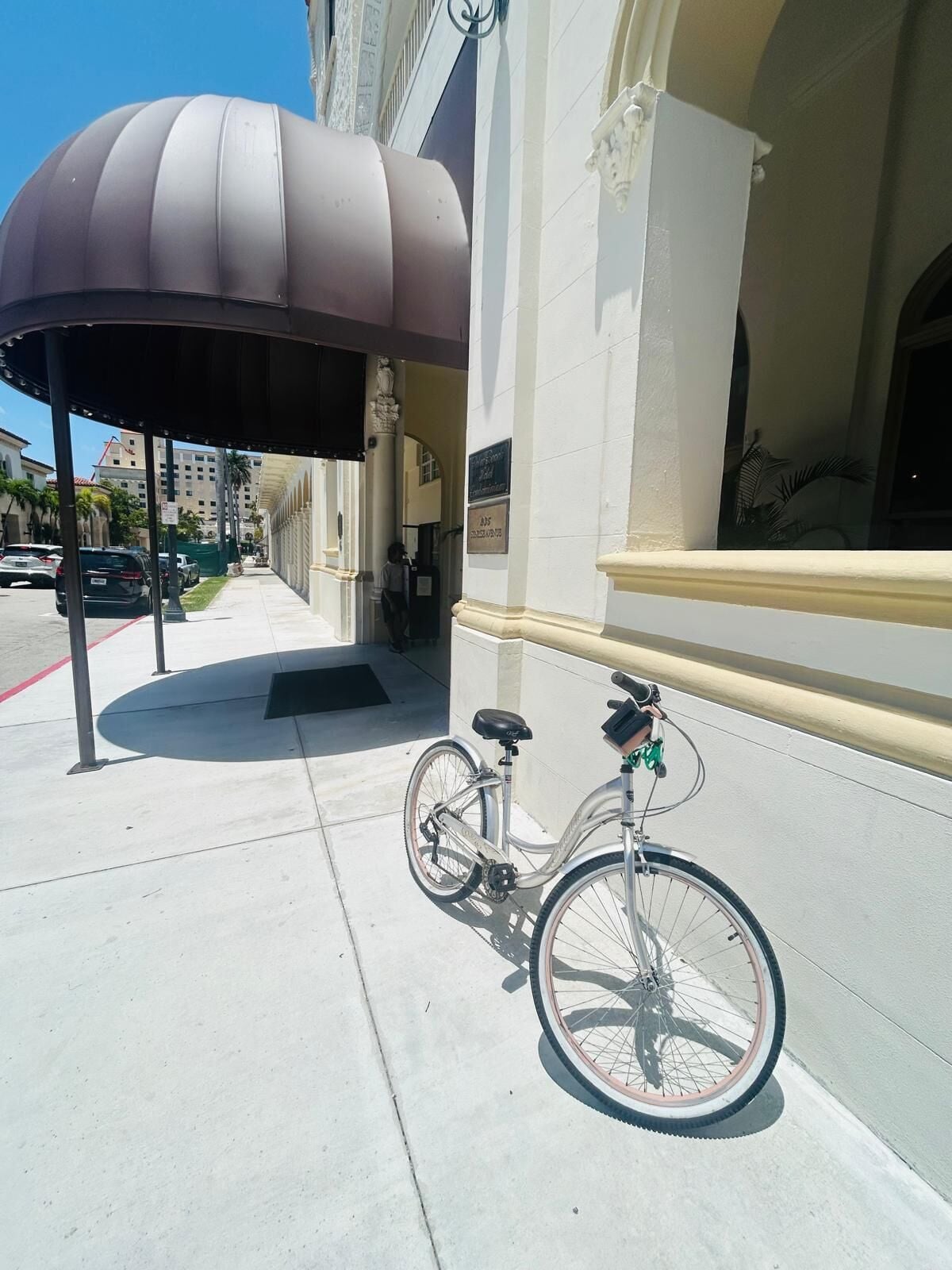 Un vélo est garé sur un trottoir, à côté d’un immeuble dont l’entrée est abritée.