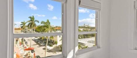A room with a bed, two windows, and a view of palm trees and a parking lot.