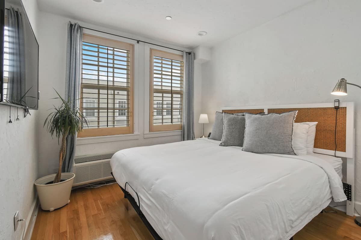 Ein Schlafzimmer mit einem großen Bett, einer Topfpflanze und einem Fenster mit Jalousien.