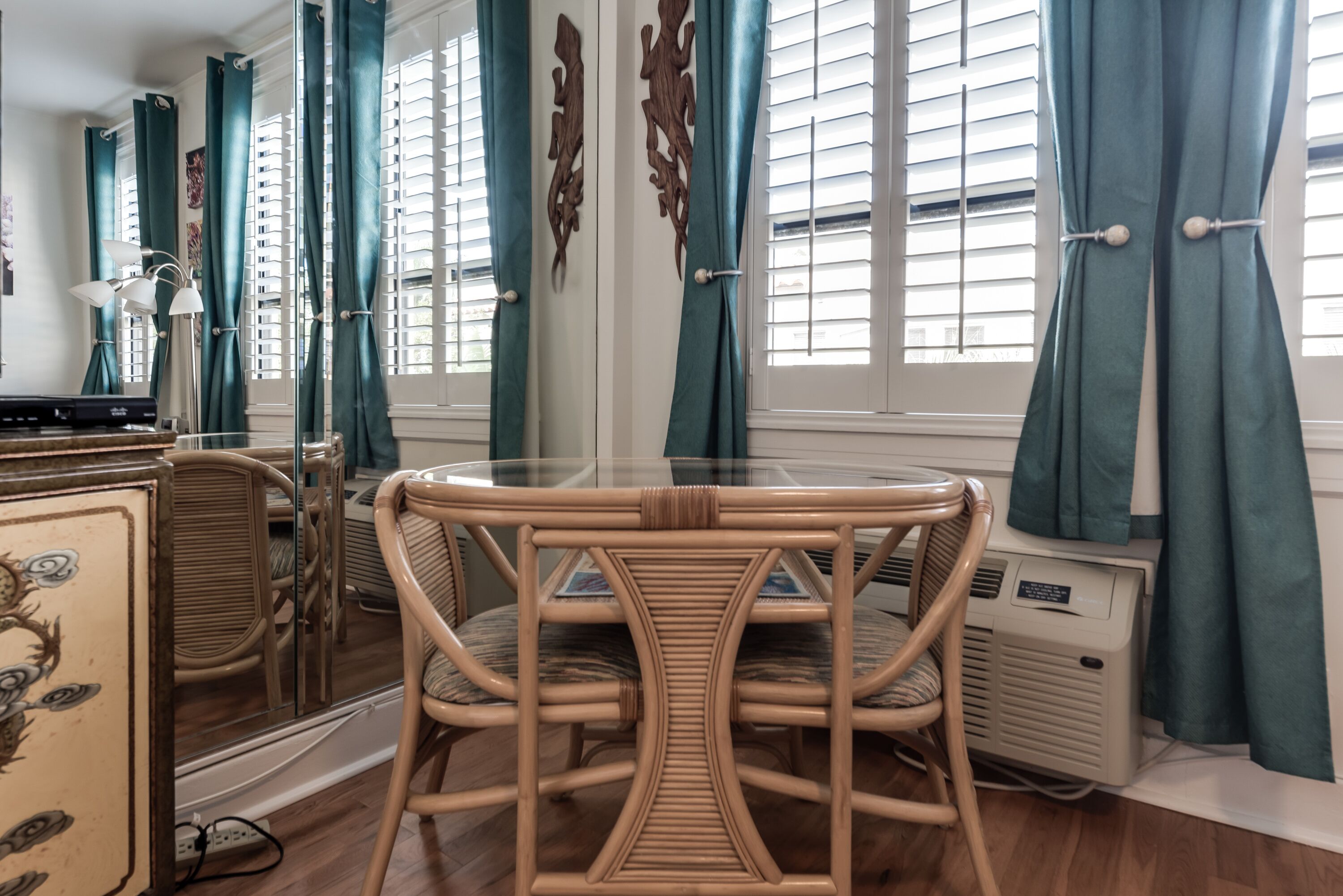 A room with a wicker chair, a table, and a mirror reflecting the room.