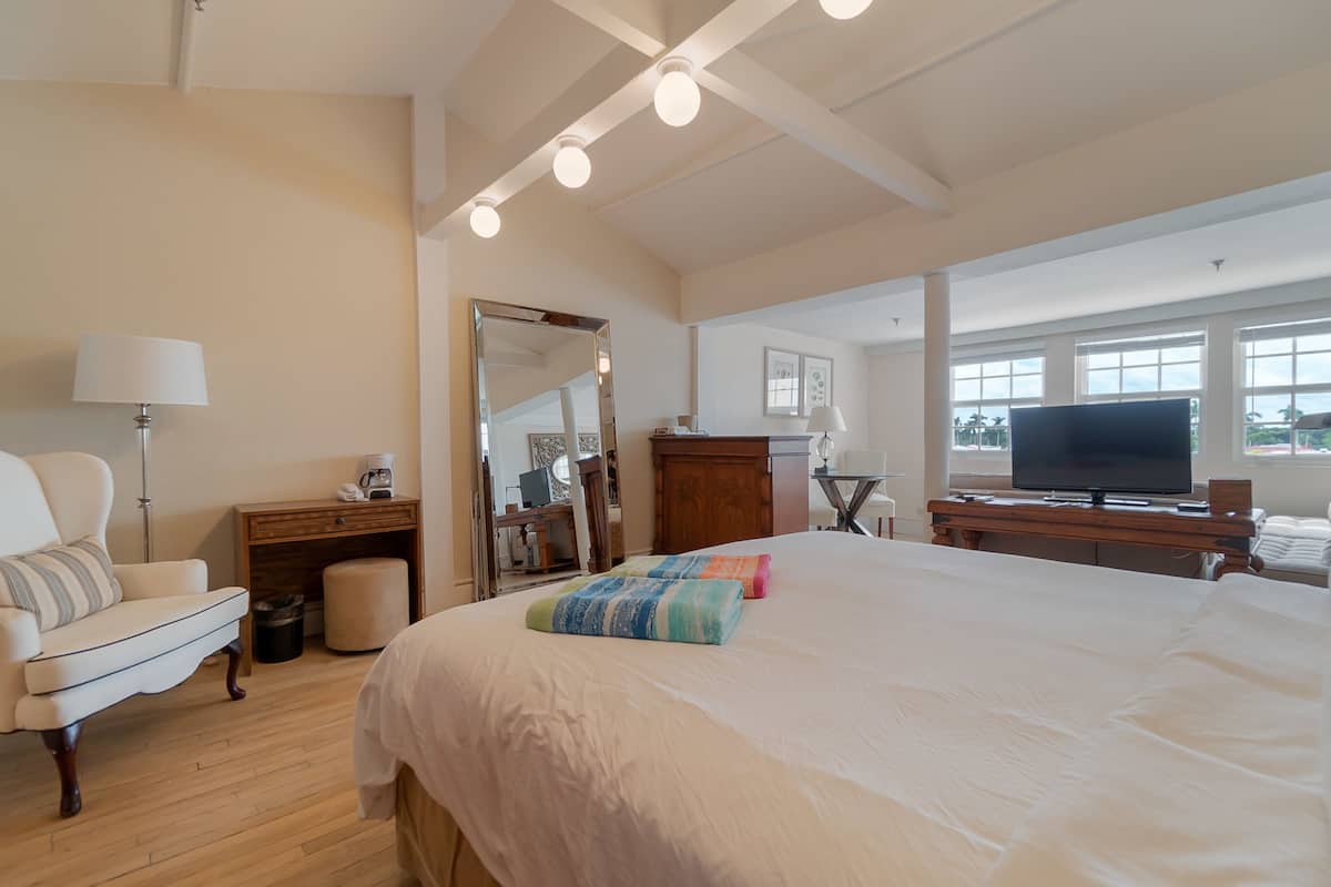 Ein geräumiges Schlafzimmer mit einem großen Bett, einem Sessel, einem Schreibtisch, einem Fernseher und einem Fenster mit Blick.