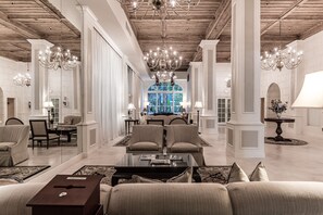 A spacious lobby with high ceilings, chandeliers, and a central seating area with sofas and a coffee table. - Tropicals of Palm Beach Condominium (Palm Beach)