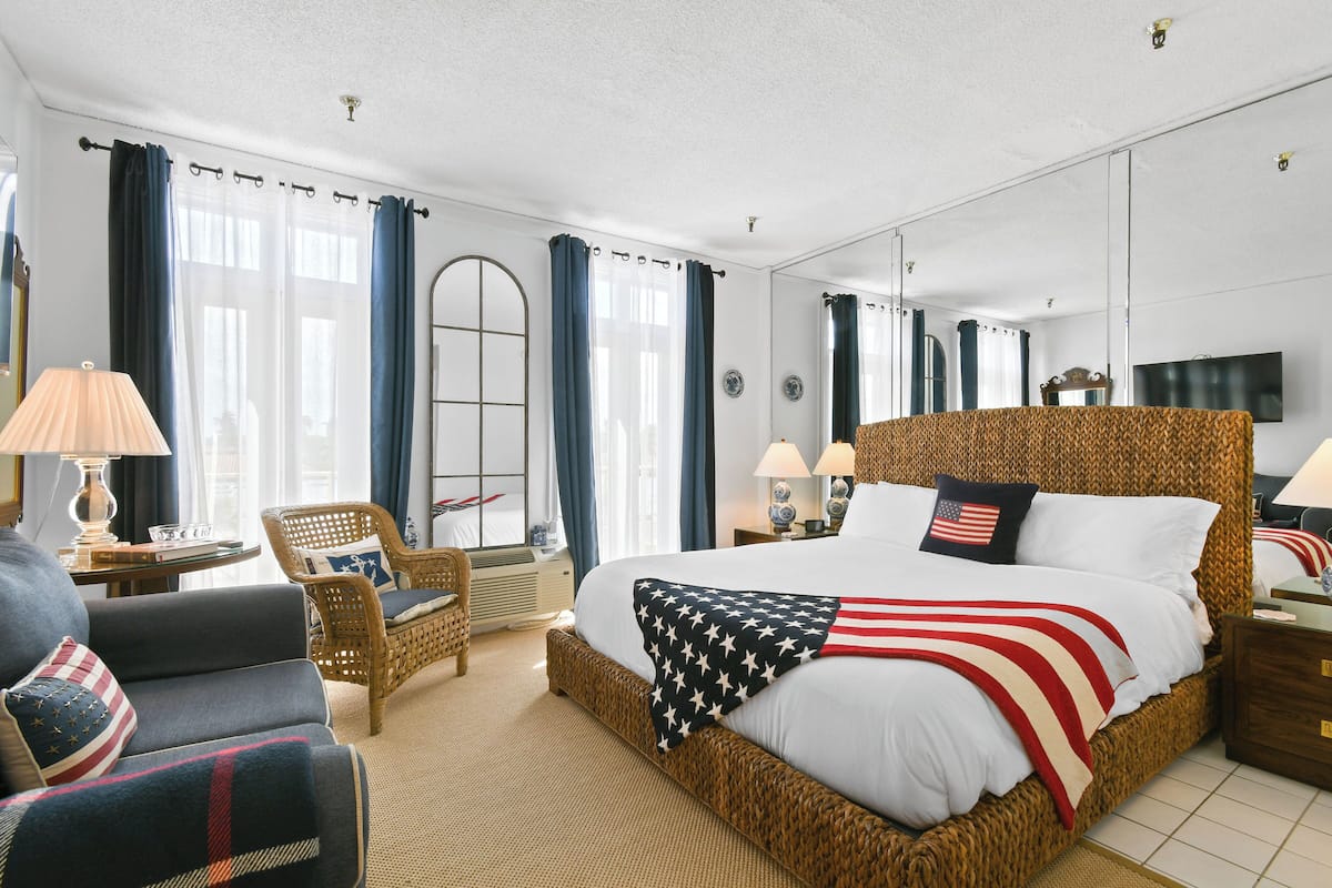 Ein Hotelzimmer mit einem großen Bett, einem Sessel, einer Lampe, einem Fernseher und einem Spiegel.
