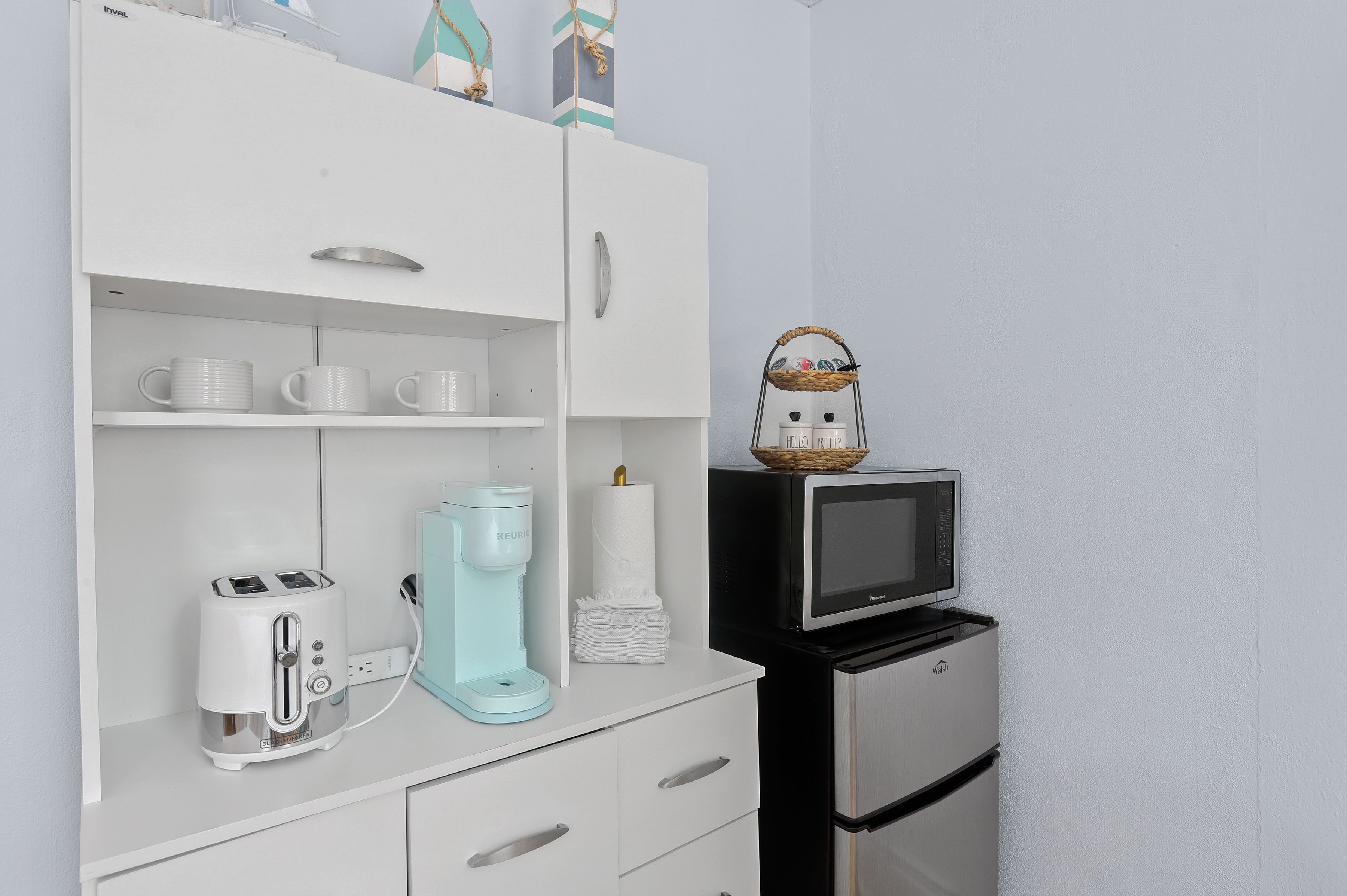Una kitchenette con un armario blanco, un tostador, una cafetera, un microondas y un refrigerador pequeño.