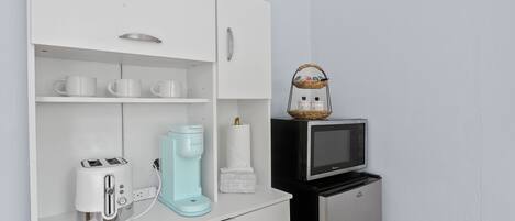 Una kitchenette con un armario blanco, un tostador, una cafetera, un microondas y un refrigerador pequeño.