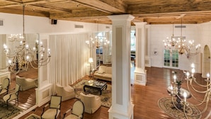 Eine geräumige Lobby mit hohen Decken, Holzbalken und Kronleuchtern. Es gibt mehrere Sitzbereiche mit Sofas und Sesseln, und einen Couchtisch in der Mitte.