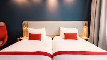 Une chambre d’hôtel avec deux lits, chacun agrémenté de draps blancs et de touches de couleur rouge, d’une tête de lit en bois, de lampes de chevet et d’une chaise rouge.