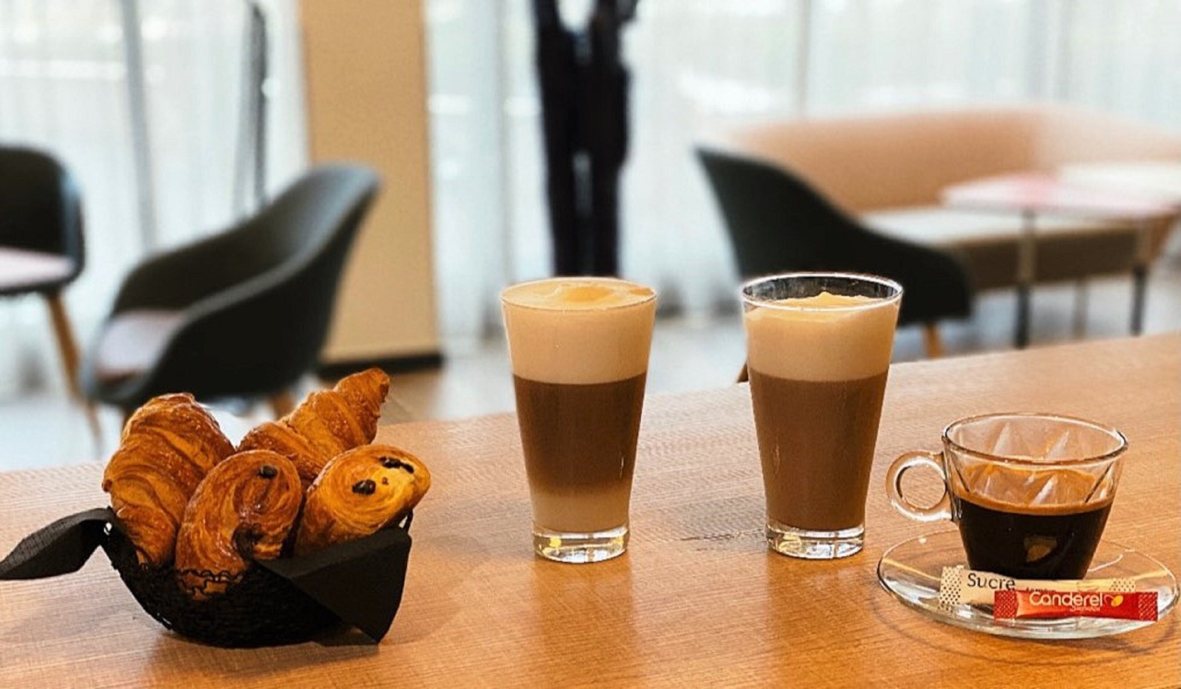 A table with pastries, two cups of coffee, and a packet of sugar.