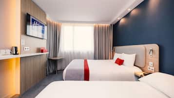Ett hotellrum med två sängar, en TV, ett skrivbord med en kaffebryggare och ett fönster med gardiner.
