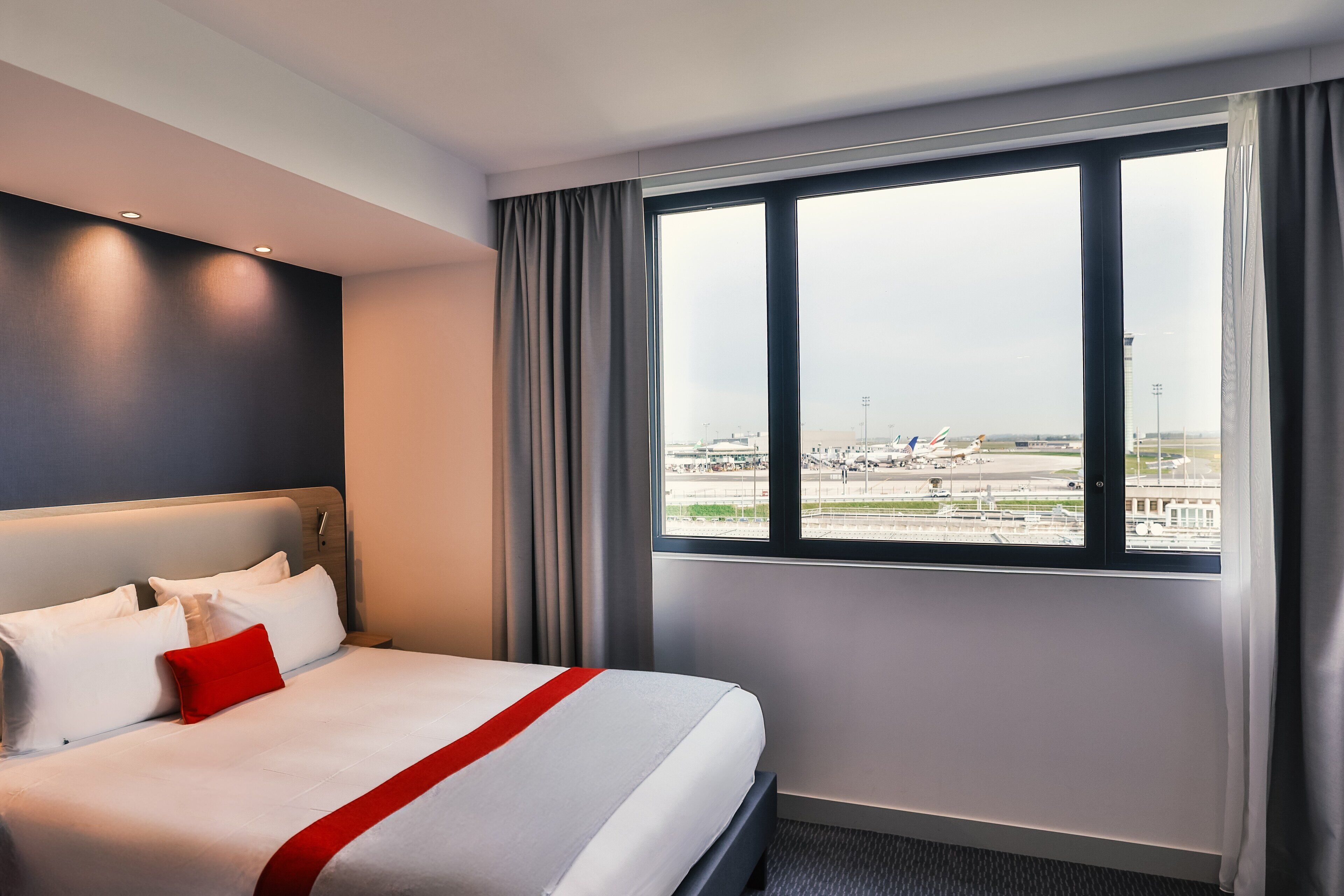 A hotel room with a large bed, a view of the airport, and a modern design.