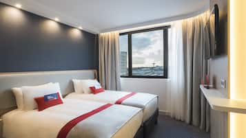 Habitación de hotel con dos camas, un ventanal con cortinas, un televisor de pantalla plana y una mesita.