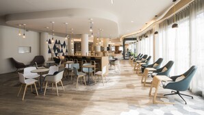 Un hall d’hôtel moderne doté d’un plafond incurvé, de plusieurs espaces de détente et d’un bar.