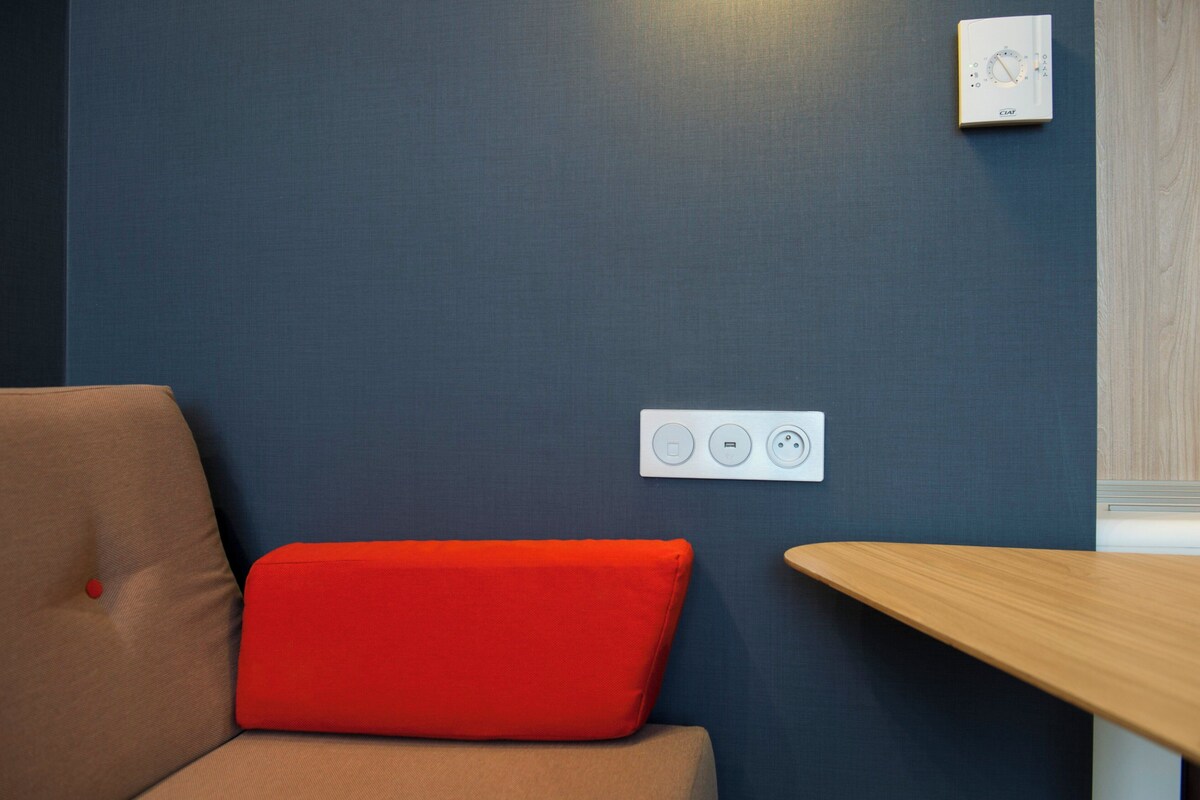 A room with a blue wall, a red cushion on a beige sofa, and a wooden table.
