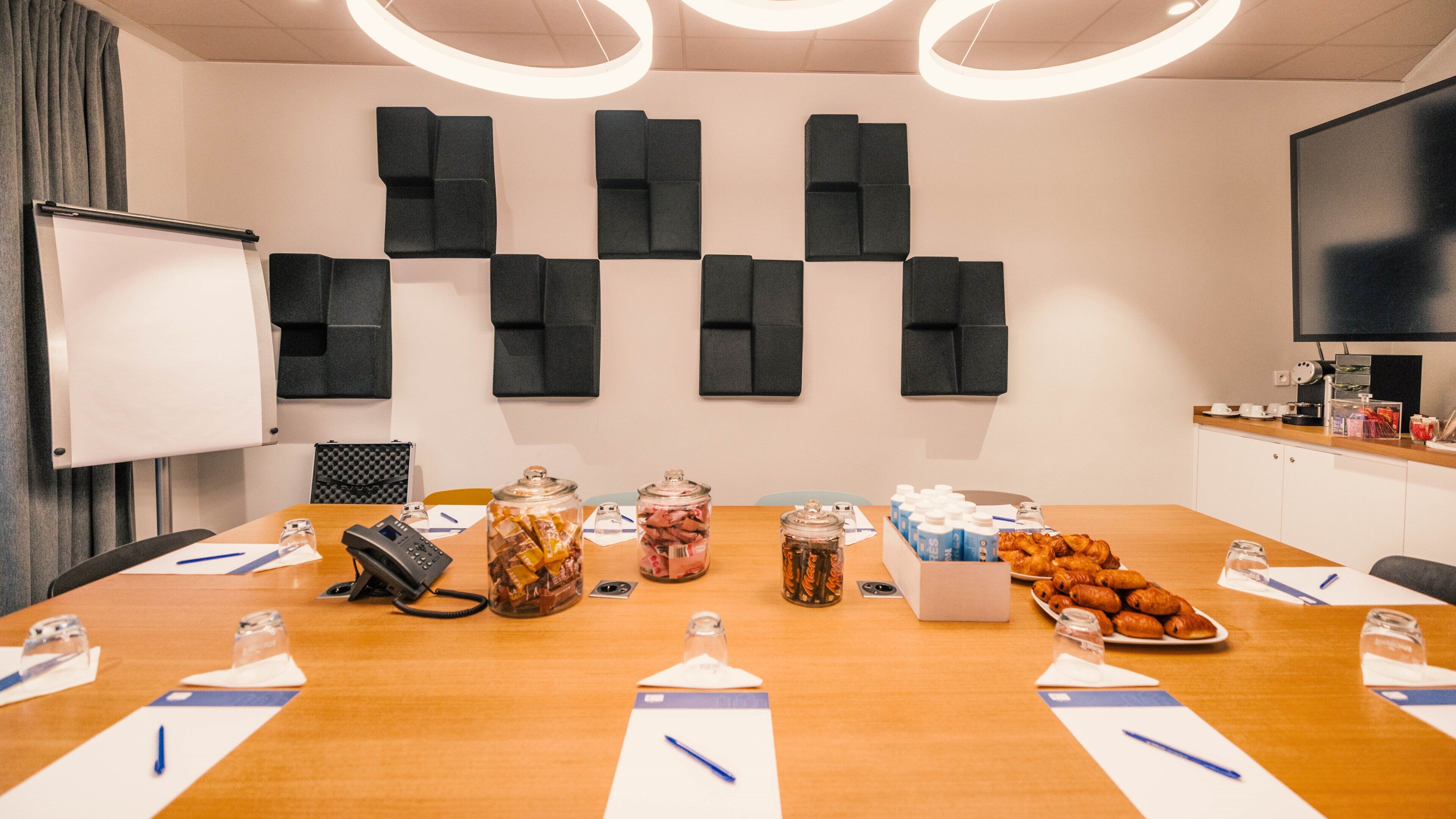 Une salle de conférence équipée d’une longue table, d’un tableau blanc et de panneaux d’insonorisation aux murs.