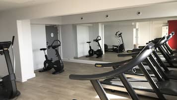 A gym with multiple treadmills and stationary bikes, a wooden floor, and a mirror reflecting the equipment.