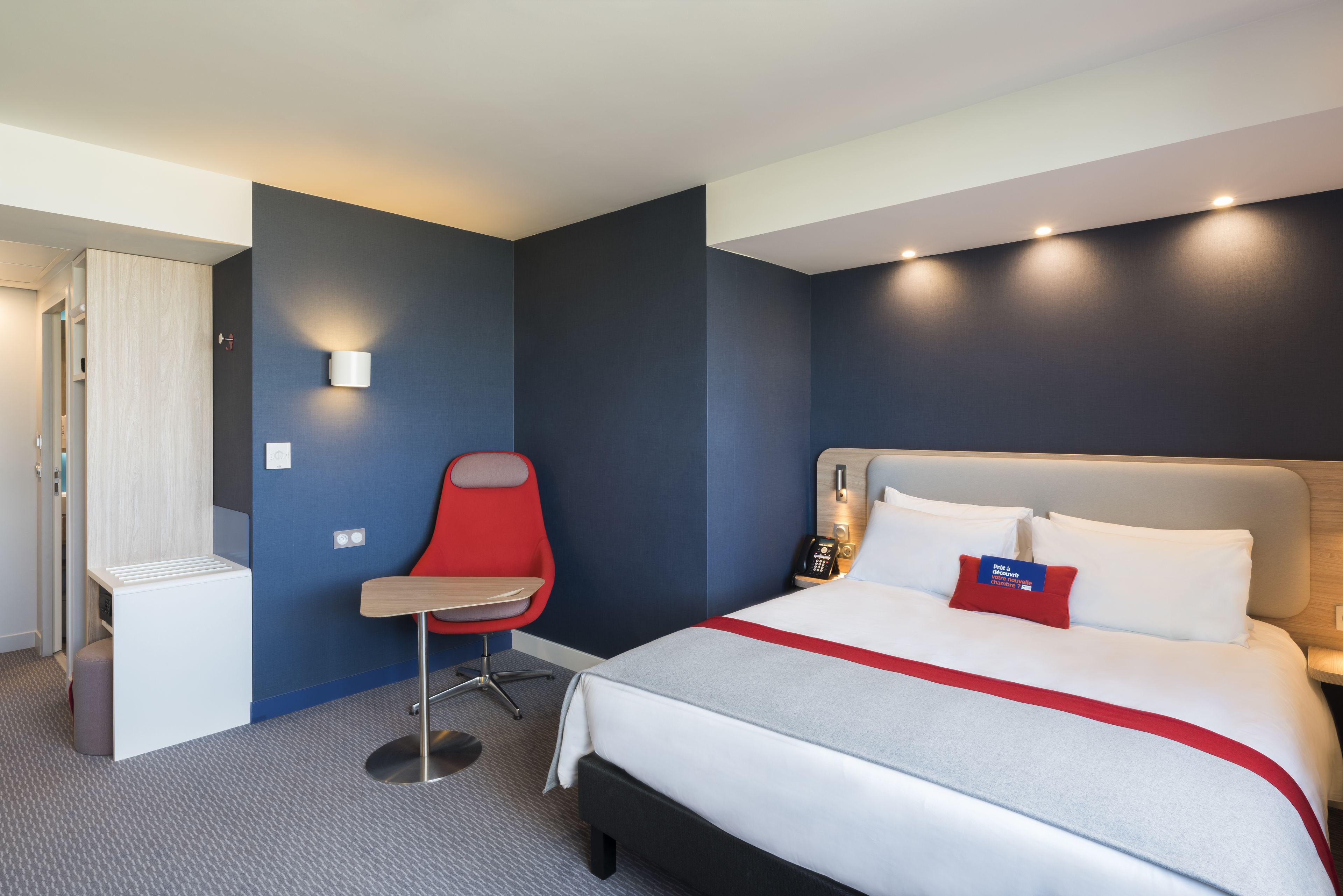Una habitación de hotel con cama, escritorio, silla, armario y mesita de noche.