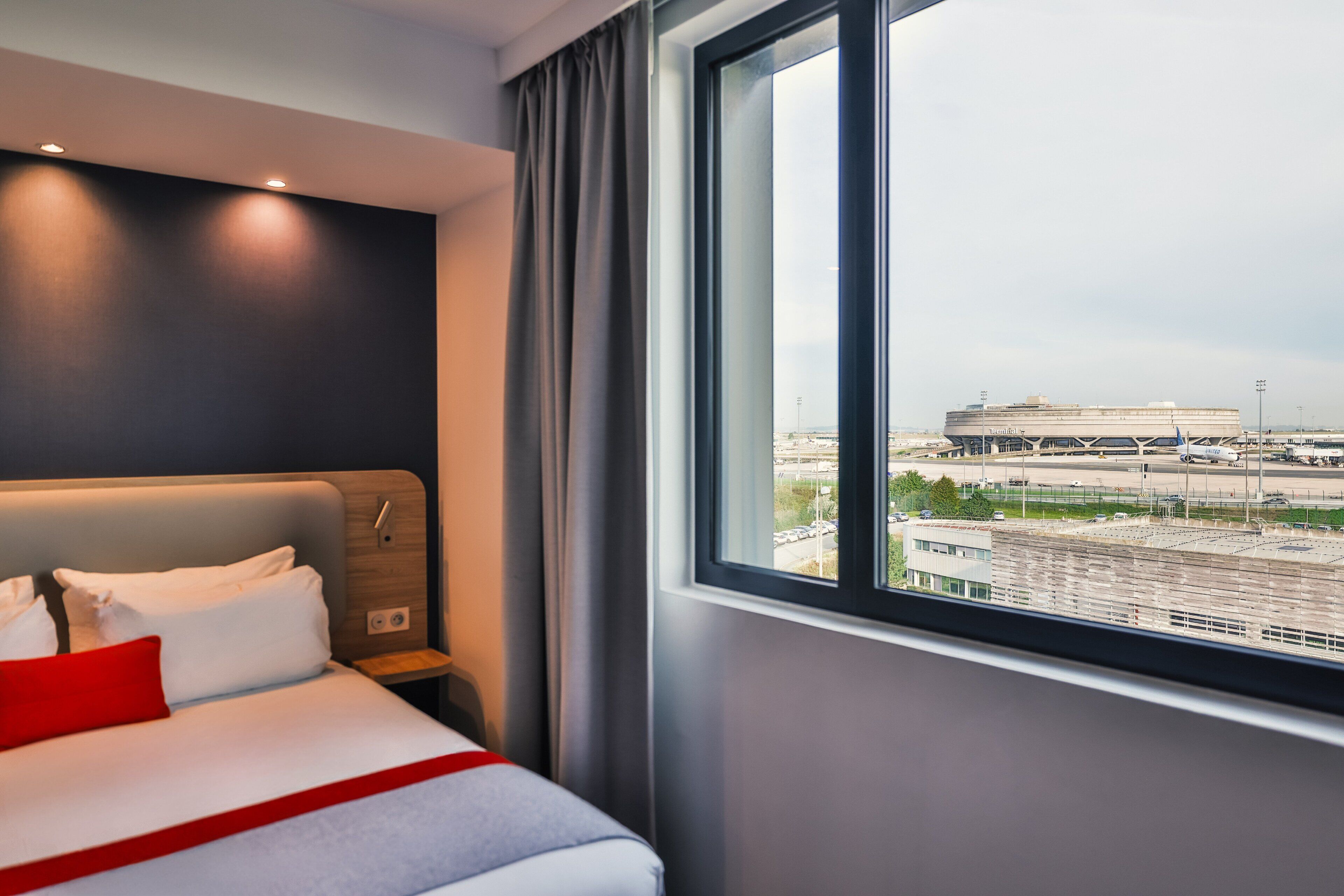 A hotel room with a bed, a window with a view of an airport, and a nightstand.
