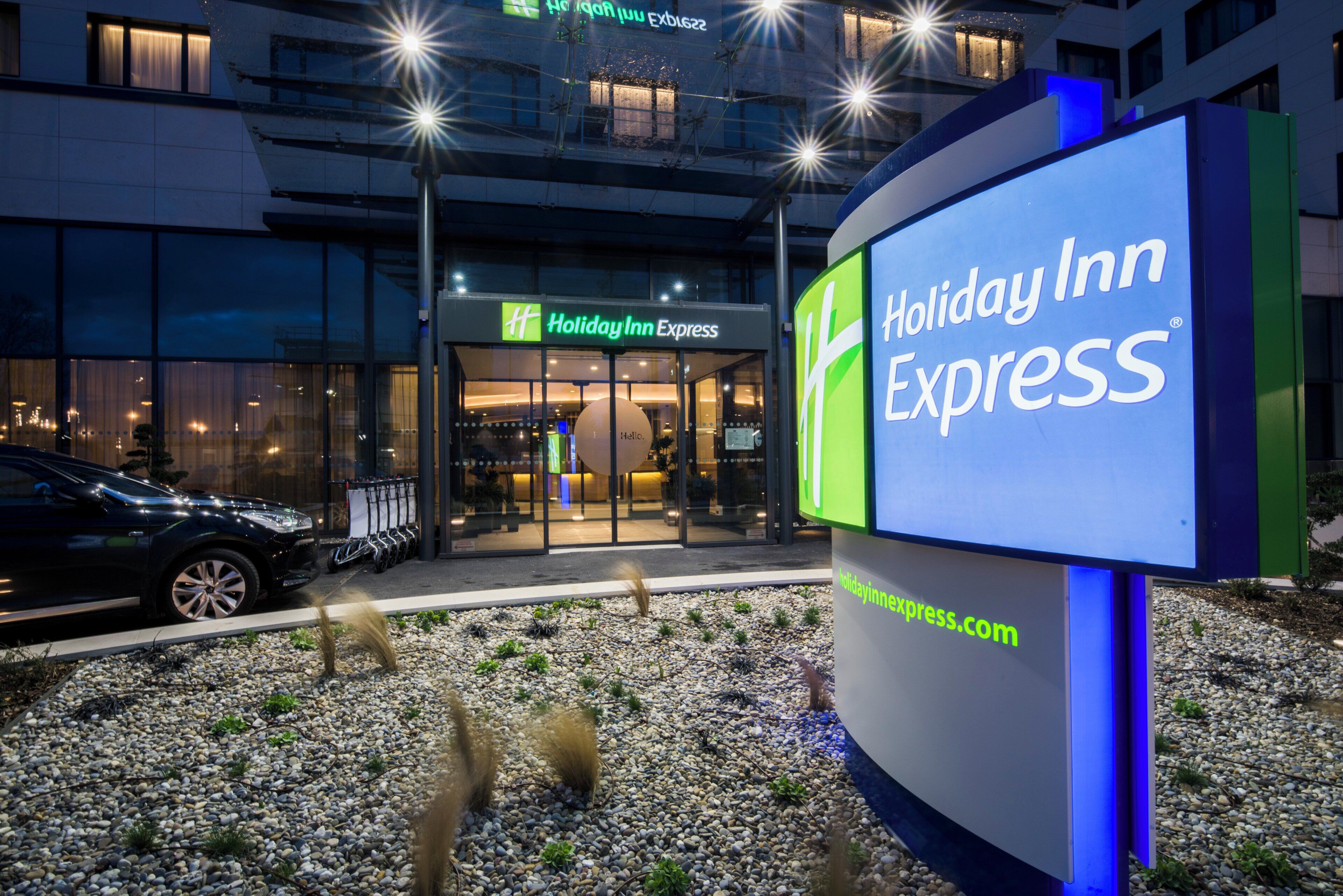 Een Holiday Inn Express gebouw met een groot verlicht bord, een parkeerplaats en een auto ervoor.