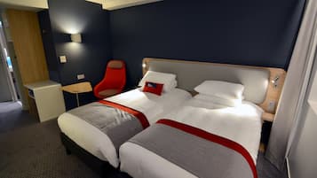A hotel room with a large bed, a red chair, a small desk, and a wall-mounted light.