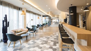Un hall d’hôtel moderne avec un long comptoir d’accueil, des sièges confortables et un sol orné d’un motif hexagonal.