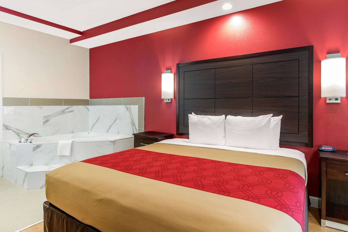 A hotel room with a large bed, a separate bathroom with a bathtub, and a red accent wall.