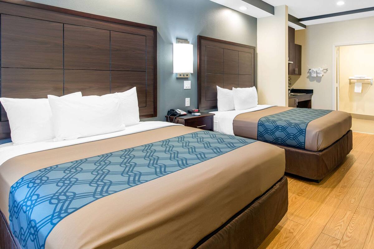 A hotel room with two beds, a nightstand, a desk, and a bathroom.